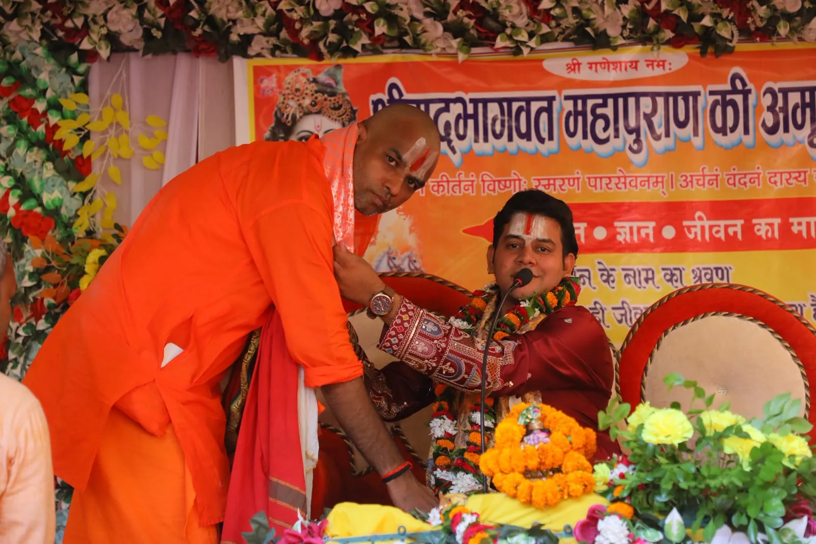 कथा मंच पर भगवा वस्त्र पहने अतिथि के साथ आचार्य अभिषेक मिश्रा